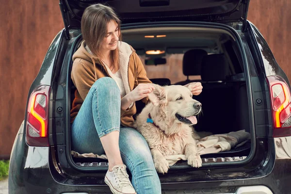 Donna con cane seduta nel bagagliaio aperto della macchina nera — Foto Stock