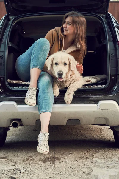 Donna felice guardando laterale mentre abbraccia golden retriever nel bagagliaio aperto di auto nera. — Foto Stock