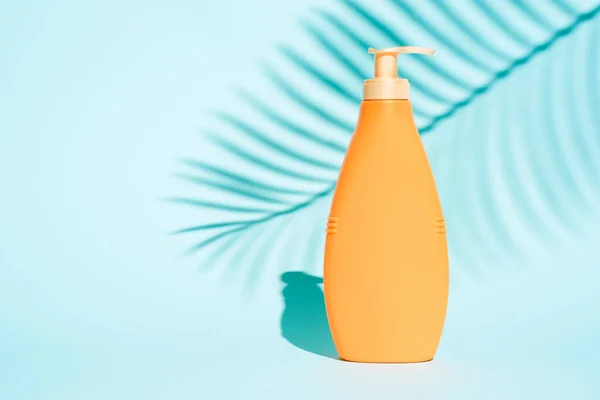 Orange container for lotion without label on blue background with leaf of fern — Stock Photo, Image