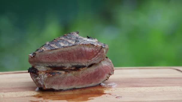 ジューシーな熱いステーキのグリル ロースト中に撮った緑の背景に木の板にあります — ストック動画