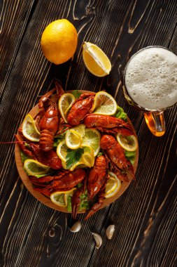 Bir tabak sıcak haşlanmış kerevit, bir bardak bira, limon, sarımsak dokulu bir kahverengi ahşap üstüne yalan ile üstten görünüm.