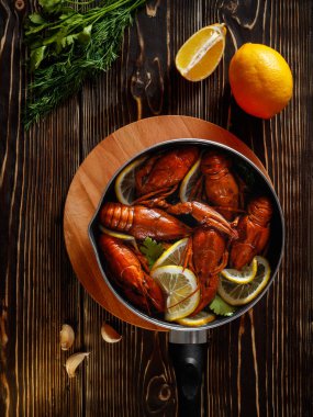 Haşlanmış kerevit ile bir tavada bir dokulu kahverengi ahşap masa üstünde duruyor. Yukarıdan görüntüleyin. Ayrıca masada bir limon, sarımsak, dereotu yeşil ve maydanoz yalan.