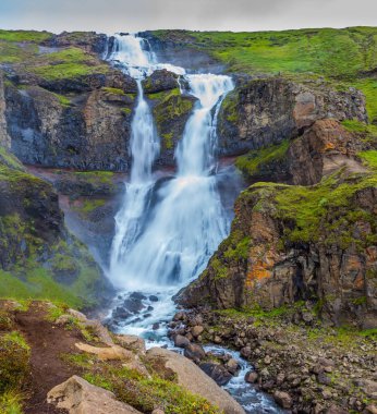 Powerful streams of cascade falls with roar breaking against cold rocks, Iceland. clipart