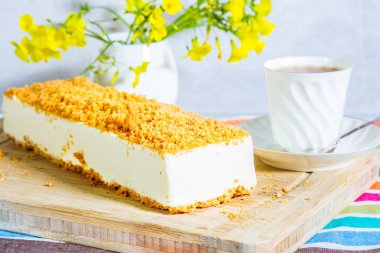 Beyaz peynirli kek, tatlı kırıntıları ile çiçekli vazo ve porselen fincan sıcak çay ile serpilir.