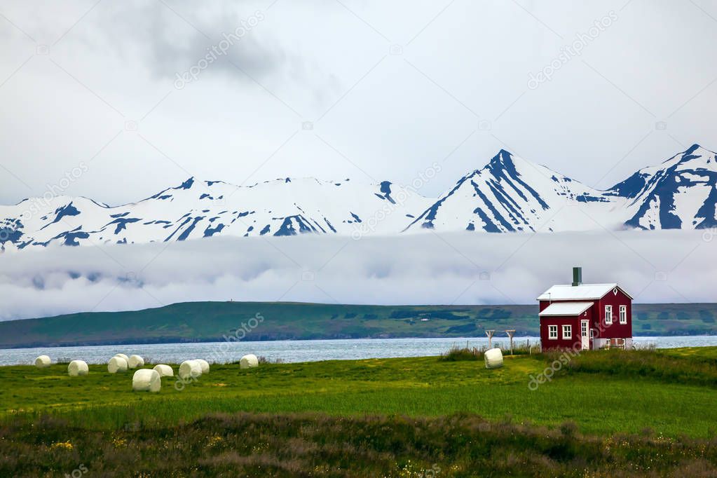 Mountains covered with snow and small farm with red walls on banks of fjord.