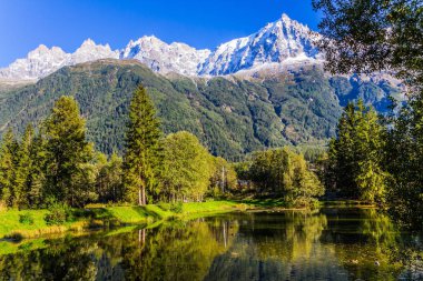 Şehir Parkı günbatımında aydınlatılır. Aktif ve ekolojik turizm kavramı. Chamonix - Mont Blanc dağ tatil. Herdem yeşil çam ve karla kaplı Alpler göle yansıyan