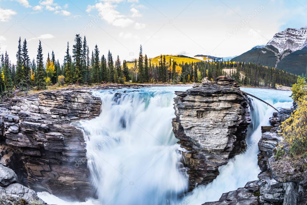 The full-water bubbling waterfall of Athabasca. Clear autumn evening in Jasper National Park. Cold blue water at sunset. The concept of extreme and ecological tourism