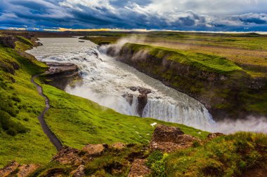 İzlanda 'daki fantastik Altın Şelale Gulfoss. Şelalenin kıyısında turistler için bir patika var. Rüzgarlı bir yaz günü. Ekstrem ve fototürizm kavramı