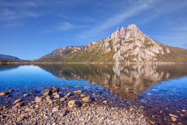 Picturesque mountain in San Carlos de Bariloche, Argentina. The water of shallow lake reflects sharp rocks. The concept of exotic and extreme tourism clipart