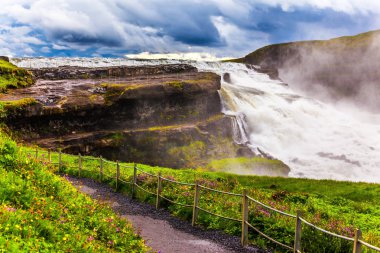 Şelale sahilde turistler için bir yoldur. İnanılmaz altın Falls - İzlanda'daki Gulfoss. Rüzgarlı ve bulutlu yaz günü. Aşırı ve phototourism kavramı