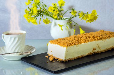 Vazoda papatyalar ve porselen fincan sıcak çay ile. Beyaz peynirli kek, turuncu tatlı kırıntıları ile serpilir