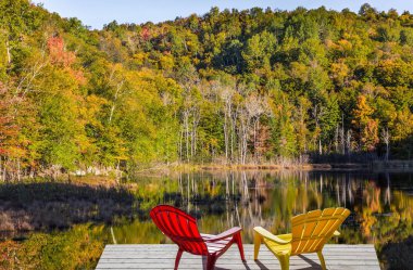 Kırmızı ve sarı şezlong gölün kıyısında. Fransızca Kanada - Mont Tremblant muhteşem beldesinde. Yeşillik ormanların gölette yansıtılır. Ekolojik turizm kavramı