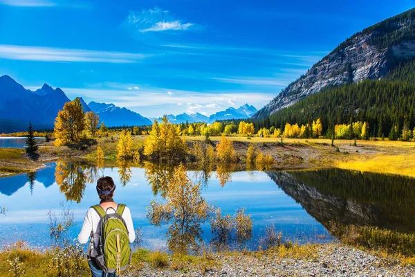 Shores of Abraham Lake in the Rocky Mountains of Canada. Middle-aged woman with a large green tourist backpack admires the lake. Concept of active, ecological and photo tourism