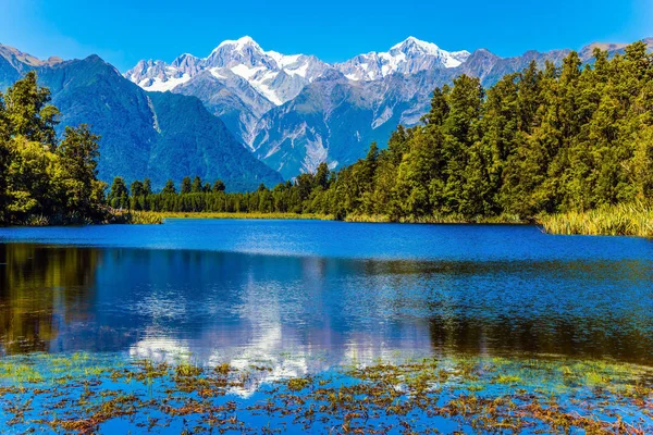 The concept of photo and ecological tourism. The snow-capped peaks of Mount Cook and Mount Tasman around the blue Lake Matheson