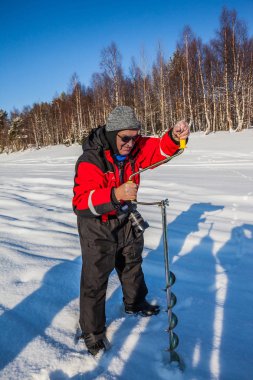 Yaşlı bir adam buz balıkçılığı için delik açar.