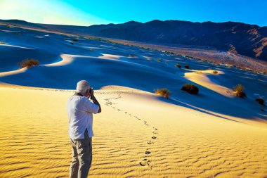 Gri saçlı adam - beyaz tişörtlü turist muhteşem manzara fotoğrafları. Gün batımı. Mesquite Düz Kum tepeleri, Ölüm Vadisi, Kaliforniya. ABD. Etkin ve fotoğraf turizmi kavramı