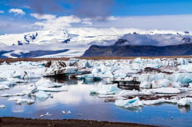 Temmuz 'da soğuk bir gün. Kuzey Kutup Dairesi, İzlanda. Suya yansıyan beyaz ve mavi buzdağları ve buz kütleleri. İzlanda. Jokulsaurloun gölü. Ekstrem, kuzey ve fotoğraf turizmi kavramı