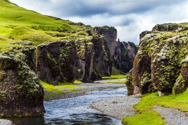 Yeşil yosunlarla kaplı uçurumlar derenin kanalını erimiş suyla kaplıyor. İzlanda. Fyadrarglyufur Kanyonu 'nun başlangıcı. Çevre, aktif ve fotoğraf turizmi kavramı