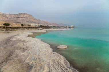 Gök mavisi deniz suyu iyileştirici tuzlarla doludur. Suda buharlaşmış tuzun küçük adacıkları. Sabahın erken saatlerinde Ölü Deniz 'in tatil köylerinde. İsrail. Ekolojik, tıbbi ve fotoğraf turizmi kavramı