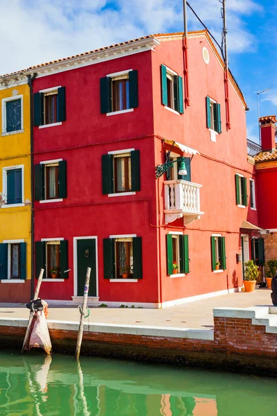 Island of Burano near Venice. Bright houses are reflected in the smooth water of the canals - streets. Facade of raspberry colored house. The concept of cultural, historical and photo tourism