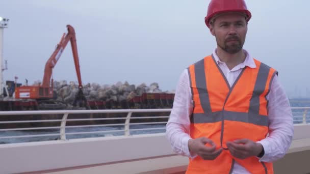 Man in een helm, architect, ingenieur, manager vertelt over reparatie werkzaamheden van de kustlijn met een steen stock footage video — Stockvideo