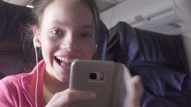 Neşeli genç kız bir oyun uçak kabin smartphone üzerinde hisse senedi görüntüleri video seyahat ederken çalış