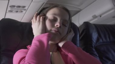 Stok görüntüleri video seyahat ederken neşeli genç kız uçak kabin kulaklıklar müzik dinler
