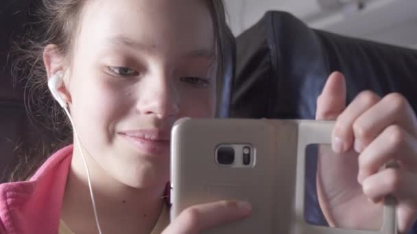 Neşeli genç kız bir oyun uçak kabin smartphone üzerinde hisse senedi görüntüleri video seyahat ederken çalış — Stok video