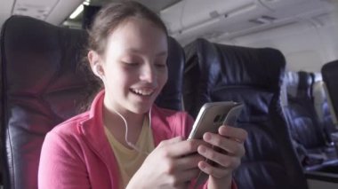 Neşeli genç kız bir oyun uçak kabin smartphone üzerinde hisse senedi görüntüleri video seyahat ederken çalış