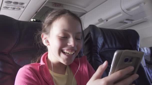 Allegro adolescente gioca a un gioco su smartphone nella cabina dell'aereo durante il viaggio magazzino filmati video — Video Stock