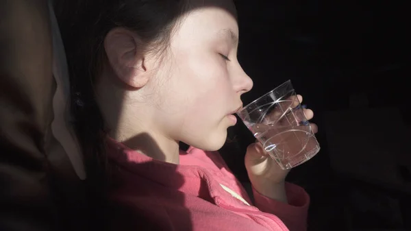 Sad teenage girl drinks water from an ailment in the cabin of plane while traveling — Stock Photo, Image