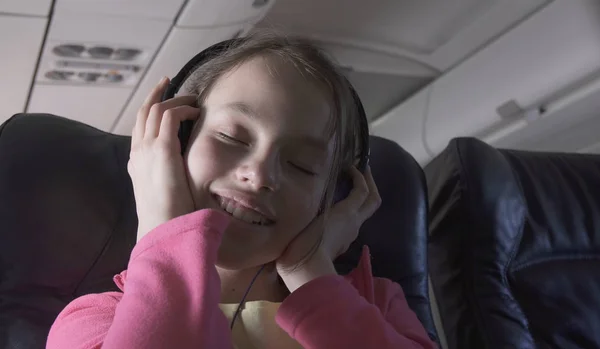 Веселая девочка-подросток слушает музыку на наушниках в салоне самолета во время путешествия — стоковое фото