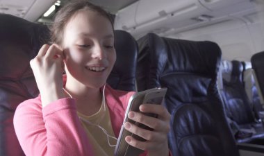 Neşeli genç kız bir oyun uçak kabin smartphone üzerinde seyahat ederken çalış