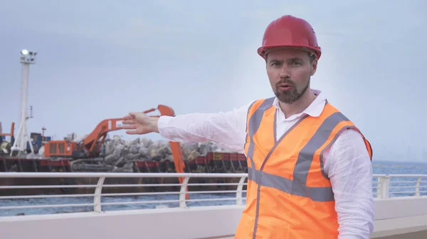 Man in een helm, architect, ingenieur, manager vertelt over reparatie werkzaamheden van de kustlijn met een steen — Stockfoto