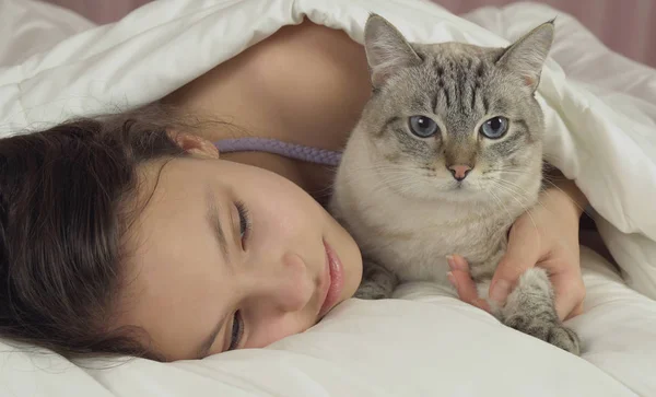 Feliz adolescente menina beija e fala com gato tailandês na cama — Fotografia de Stock