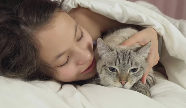 Счастливая девочка-подросток целуется и разговаривает с тайской кошкой в постели — стоковое фото