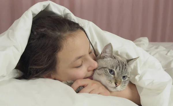 Feliz adolescente menina beija e fala com gato tailandês na cama — Fotografia de Stock