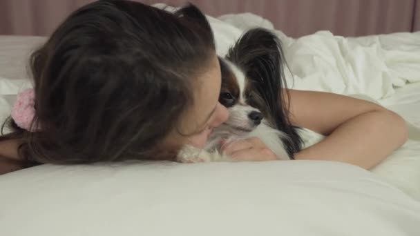 Feliz adolescente chica besos y juega con perro Papillon en la cama material de archivo de vídeo — Vídeo de stock