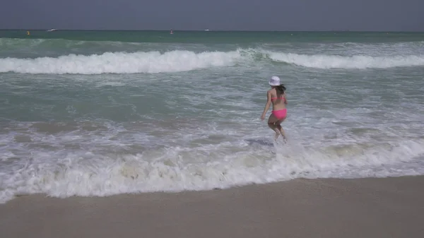 身穿游泳衣的少女在迪拜海滩上的波斯湾海浪中愉快地跳来跳去 — 图库照片