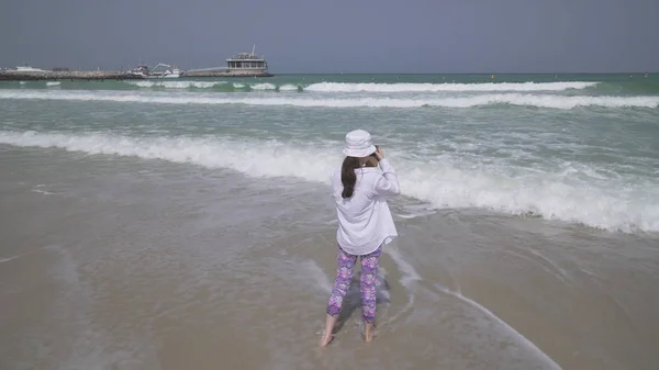 Menina adolescente dispara no smartphone as ondas do mar em Public Jumeirah Open Beach, na costa do Golfo Pérsico, Dubai — Fotografia de Stock