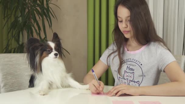 Девочка-подросток с собакой Papillon гадать о желаниях, пишет желание кусочки бумаги видео акции — стоковое видео