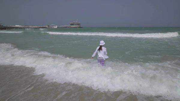 在迪拜海滩上, 穿着衣服的少女在波斯湾的波浪中快乐地跳跃 — 图库照片