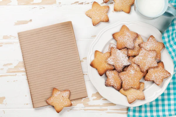 Cookies and milk on white wooden table. Top view with notepad for your text