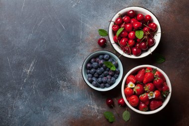 Taze yaz meyveleri. Kiraz, böğürtlen ve çilek kase karanlık taş zemin üzerine. Metin alanı olan üstten görünüm