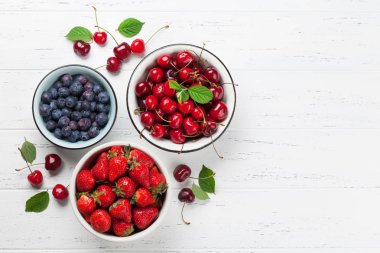 Taze yaz yaban mersini, kiraz ve çilek kase Beyaz ahşap zemin üzerinde. Metin alanı olan üstten görünüm