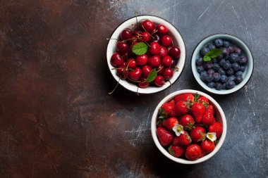 Taze yaz yaban mersini, kiraz ve çilek kase karanlık taş zemin üzerine. Metin alanı olan üstten görünüm