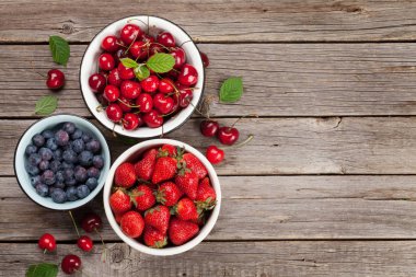 Taze kiraz, böğürtlen ve çilek kase ahşap arka plan üzerinde. Metin alanı olan üstten görünüm