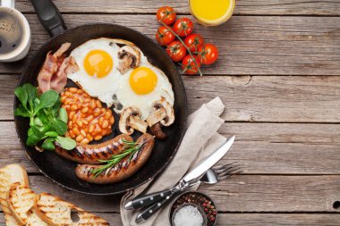 İngiliz kahvaltısı. Kızarmış yumurta, sosis, pastırma, fasulye, tost, domates, portakal suyu ve kahve fincanı ahşap masa üzerinde. Kopya alanı ile Üstten Görünüm
