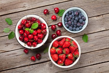 Taze yaz kiraz, böğürtlen ve çilek kase ahşap arka plan üzerinde. Üstten görünüm