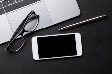 Akıllı telefon, laptop, gözlük ve kalemi siyah tablo üzerinde. Düz yatıyordu. Kopya alanı ile üstten görünüm